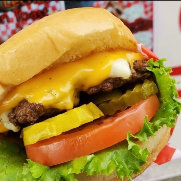 A close-up of a cheeseburger with melted cheese, pickles, tomato, and lettuce on a bun.