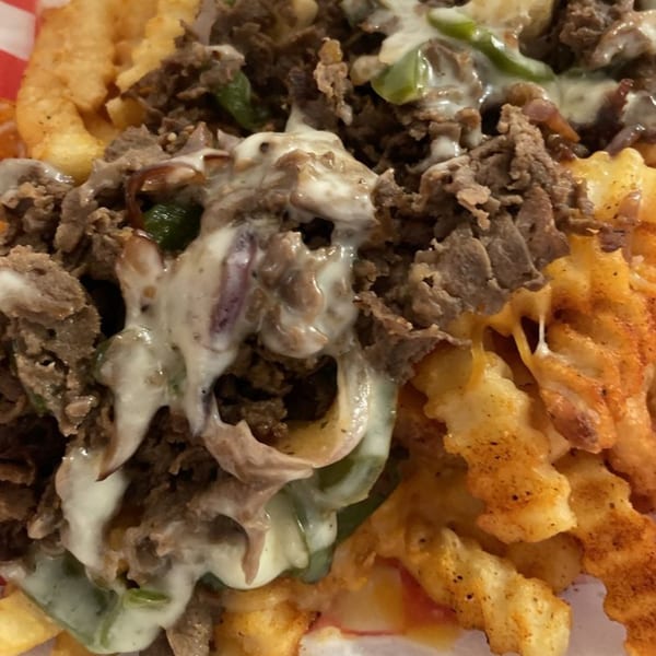Close-up of waffle fries topped with steak, green peppers, onions, and melted white cheese.