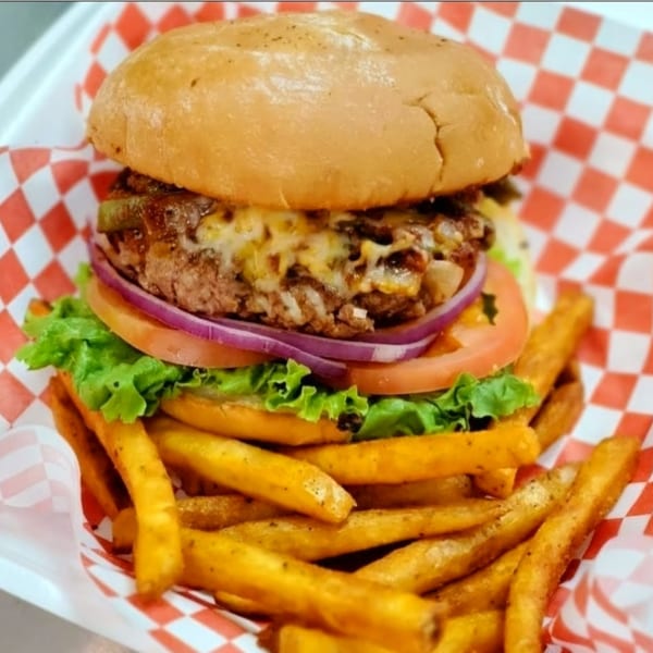 Cesar's Snack Shack burger with melted cheese, lettuce, tomato, onion, and a side of fries.