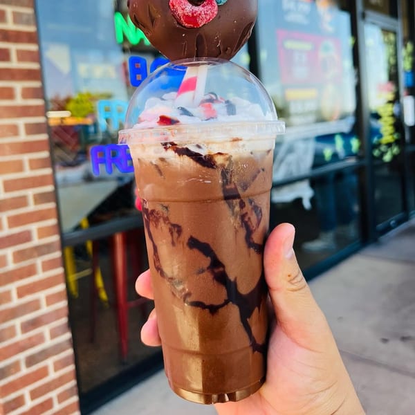 Hand holding a chocolate milkshake with whipped cream, topped with a chocolate-covered strawberry.