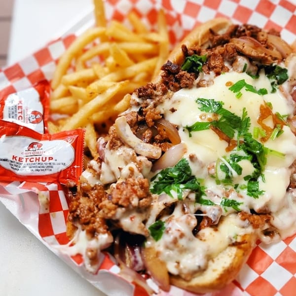 A cheesy Tex-Mex sandwich with ground meat, onions, and cilantro, served with fries and ketchup packets.