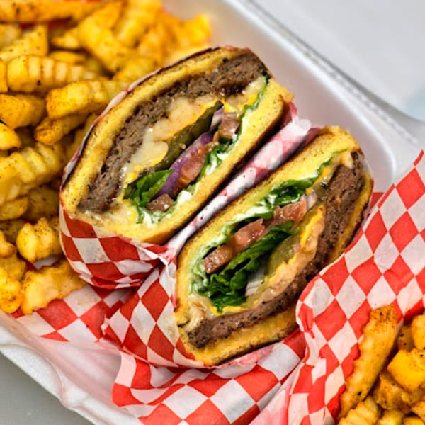 A cut-in-half burger with cheese, lettuce, tomato, and onion, served with crinkle-cut fries.