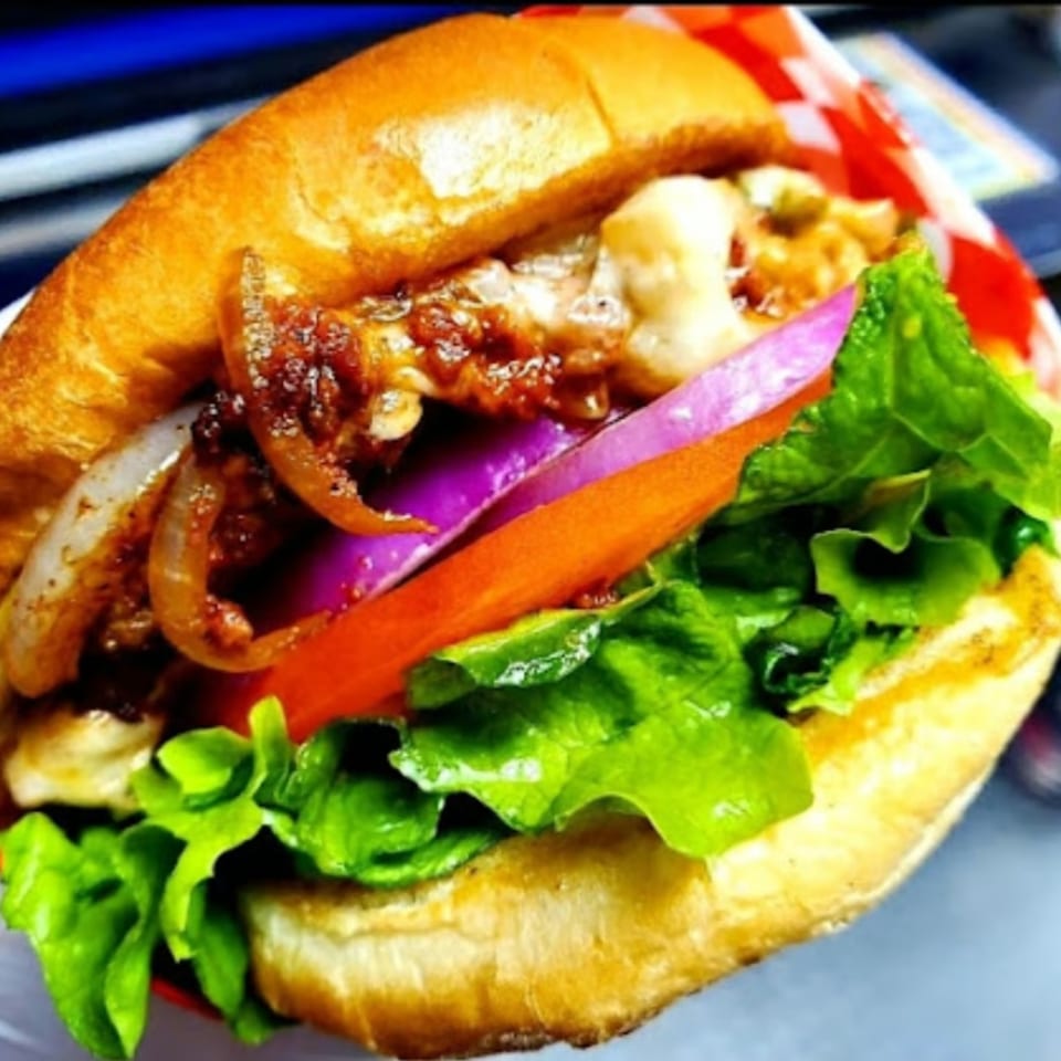 Close-up of a tex-mex burger with melted cheese, caramelized onions, red onion, tomato, and lettuce.