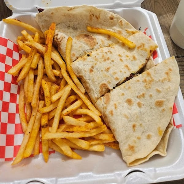 A takeout container holds a quesadilla cut in half and a generous serving of seasoned french fries.