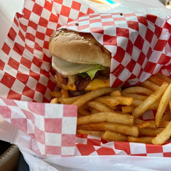 A Cesar's Snack Shack burger with cheese, bacon, lettuce, and pickles, served with fries.