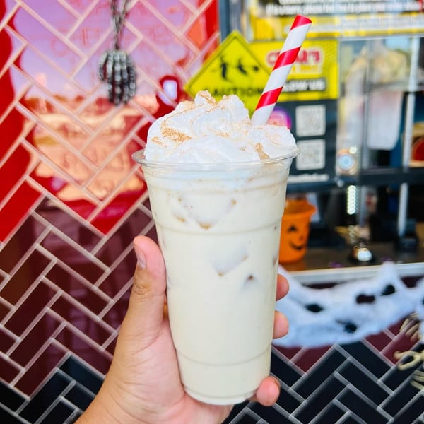 Hand holding a horchata drink with whipped cream, cinnamon, and a red and white straw.
