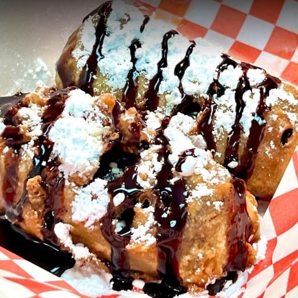 Deep-fried dessert chimichangas drizzled with chocolate sauce and powdered sugar in a red checkered basket.